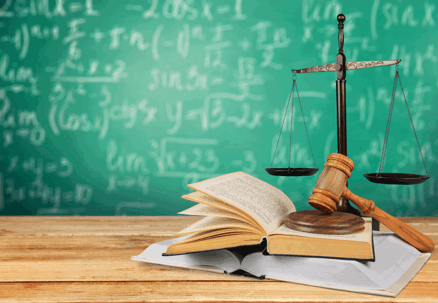 Law book and justice scales in front of a chalk board with equations.
